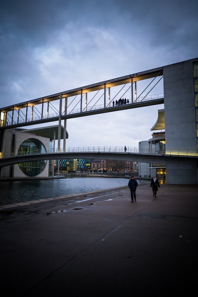 During the day, a grey sky, people walk in gray cement on the bridge
